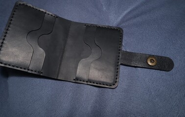 Handmade leather wallet made of black leather on a blue velor background 