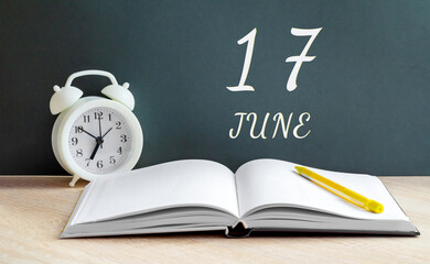 june 17. 17-th day of the month, calendar date.A white alarm clock, an open notebook with blank pages, and a yellow pencil lie on the table.Summer month, day of the year concept