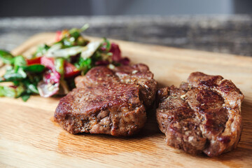 Grilled beef steaks on wooden cutting board. Tasty juicy grilled steak and salad with tomatoes on cutting board.