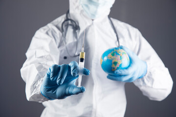 a doctor in a protective uniform holds a syringe and a globe