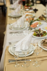 Close up of festive table setting with wine glasses, fresh flowers on beige tablecloth