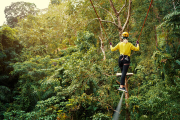 Young woman with climbing gear in an adventure extreme park climbing or passing on the rope road.