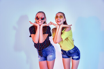 Two female teenagers in sunglasses and summer clothes posing in studio on white background