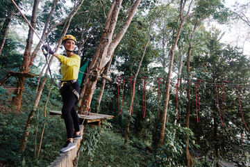 Young woman with climbing gear in an adventure extreme park climbing or passing on the rope road. - obrazy, fototapety, plakaty