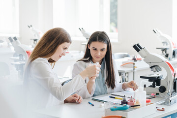 Young female researchers in white coats examining laboratory sample in science class