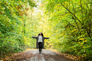 Carefree woman with arms outstretched running on footpath in forest