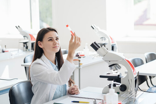 Young female researcher in white coat examining laboratory sample