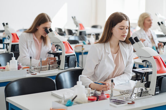 Researchers in white coats working with microscopes in lab