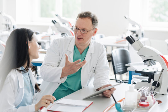 Teacher and student in white coats talking and using tablet in lab