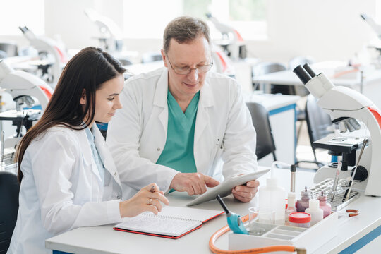 Scientists in white coats using tablet in lab