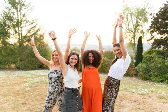 Cheerful female friends with hands raised at park