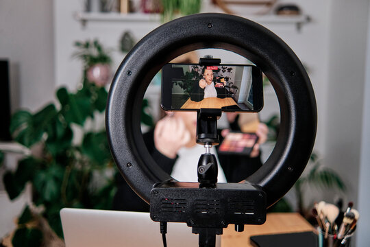 Woman applying make-up while filming make-up tutorial at home