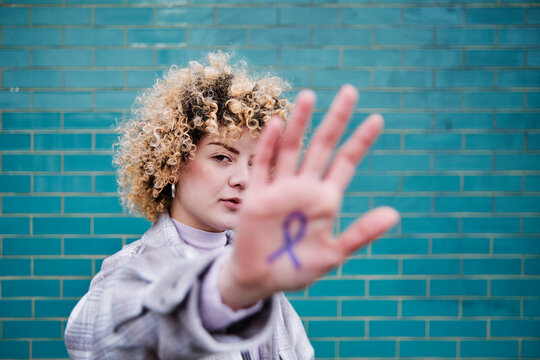 Curly haired woman showing colon cancer ribbon symbol on hand