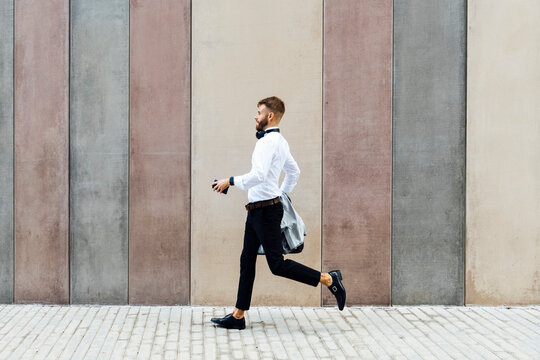 Businessman holding briefcase and jacket while running against wall