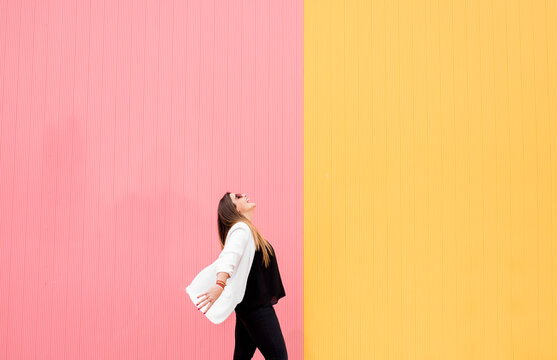 Cheerful young woman in sunglasses against pink and yellow wall