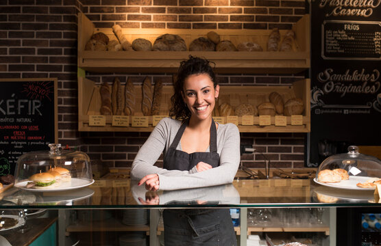 Smiling woman standing against baked food rack in illuminated bakery