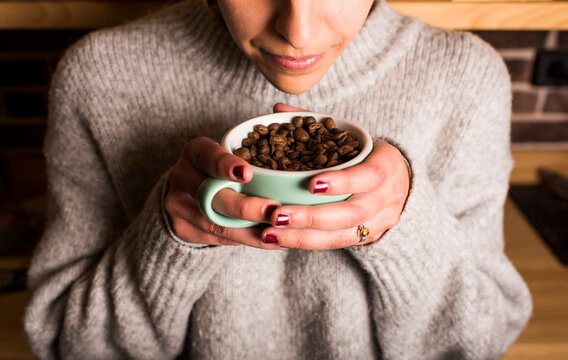 Young woman smelling fresh coffee beans in cup at cafe