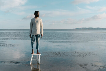Thoughtful young man looking away while standing on stool at beach during sunset