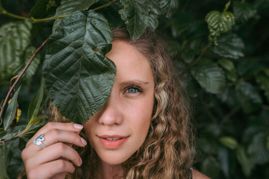 Beautiful blond woman covering eye with leaf in park