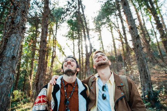 Cheerful Gay Couple Looking Up While Hiking In Forest During Vacations