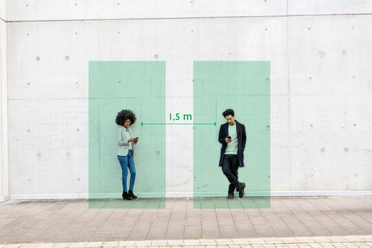 Rectangles visualizing social distancing covering man and woman standing outdoors with smart phones in hands