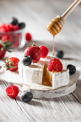 Camembert cheese with honey, raspberries, blueberries and strawberries. Honey flowing with honey stick on camembert cheese, brie cheese. The keto diet.