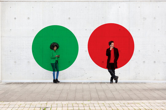 Two circles visualizing social distancing covering man and woman standing outdoors with smart phones in hands