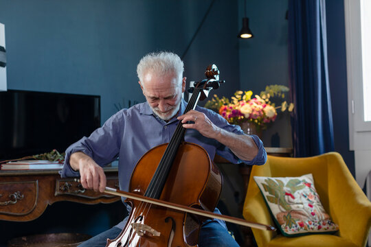 Senior man playing cello while sitting in living room at home