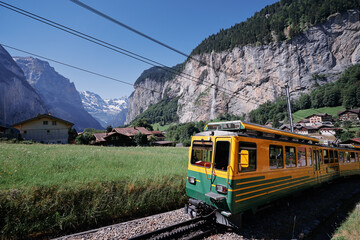 Obraz premium Beautiful mountains landscape. Yellow-green train running through the Swiss Grindelwald Village, Switzerland.