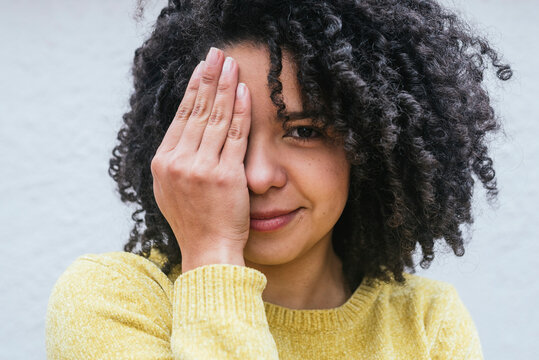 Curly haired woman covering eye against white wall