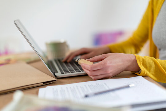 Mid adult woman holding USB stick by laptop on table at home