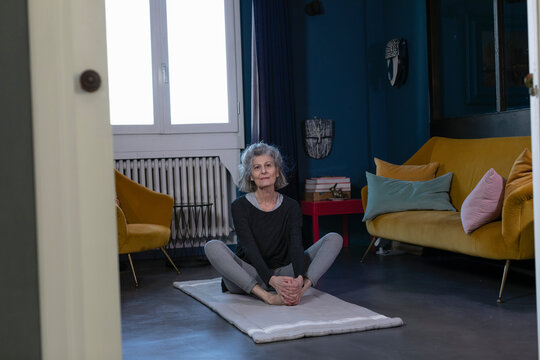 Senior woman practicing Yoga on exercise mat at home