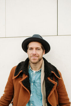 Male Hipster Wearing Coat And Hat Against White Wall