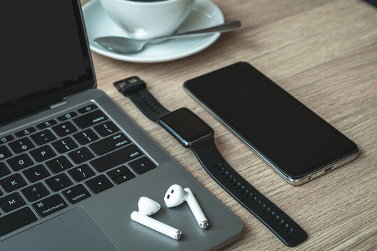 Close-up of Keyboard laptop computer, wireless earphones focus with smartwatch,Hot coffee in cup mug and smartphone empty screen on wooden background office desk in coffee shop like the background - Powered by Adobe