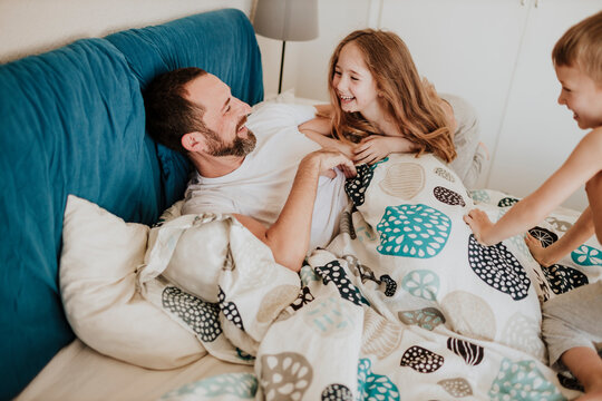 Smiling daughter and son having fun with father on bed at home