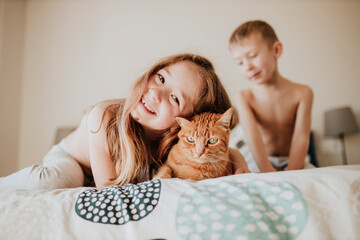 Smiling girl leaning on cat while brother in background in bedroom at home