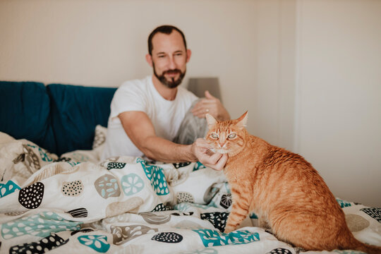 Mature Man Stroking Ginger Cat While Sitting On Bed