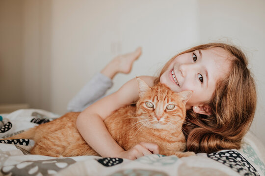 Cute smiling girl with ginger cat on bed at home