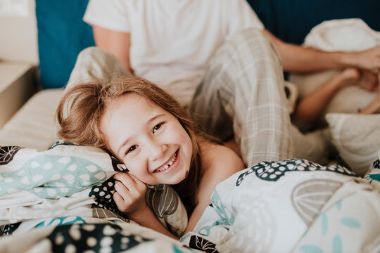 Cheerful girl lying on bed with father sitting in background at home