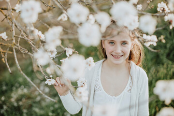 Cute girl smiling while holding branch of almond tree blossom during springtime