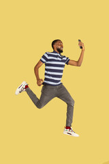 Fototapeta na wymiar One African young man jumping isolated over yellow studio background with copyspace for ad