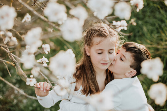 Brother kissing sister on cheek by almond blossoms