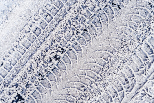 Diagonal traces of car tires in the fresh snow on the asphalt. Close up view from above