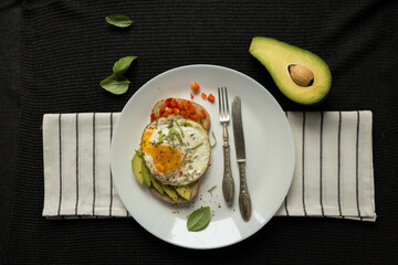 Breakfast sandwich flat lay with fried egg, avocado slices, red pepper, spices and green basil leaves, on serving plate with vintage fork. Culinary Top view with copy space. Healthy high protein diet.
