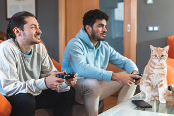 Young male friends playing video game while cat sitting on table at home