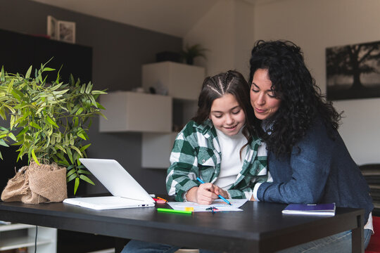 Mother assisting daughter while studying at table in living room