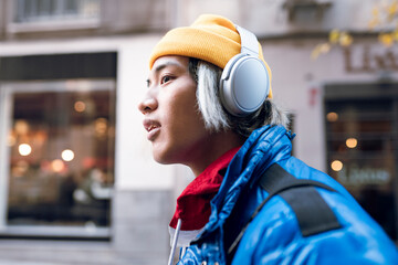 Asian man listening music through headphones outdoors