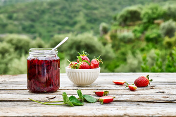 Strawberry jam in a jar and fresh red ripe organic bio strawberries in a bowl on wooden table in the garden. Spring or summer harvesting. Healthy eating. Vitamin.