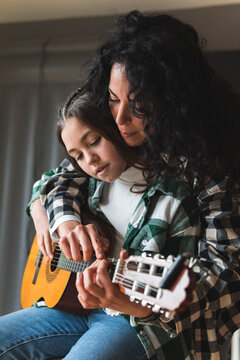 Mother teaching little daughter how to play acoustic guitar