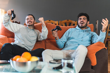 Young competitive friends playing video game sitting on sofa in living room
